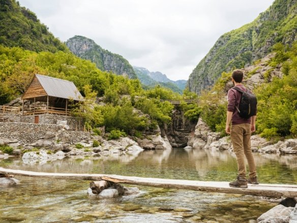 Man on wooden bridge looking at cabin, Accursed mountains, Theth, Shkoder, Albania, Europe
